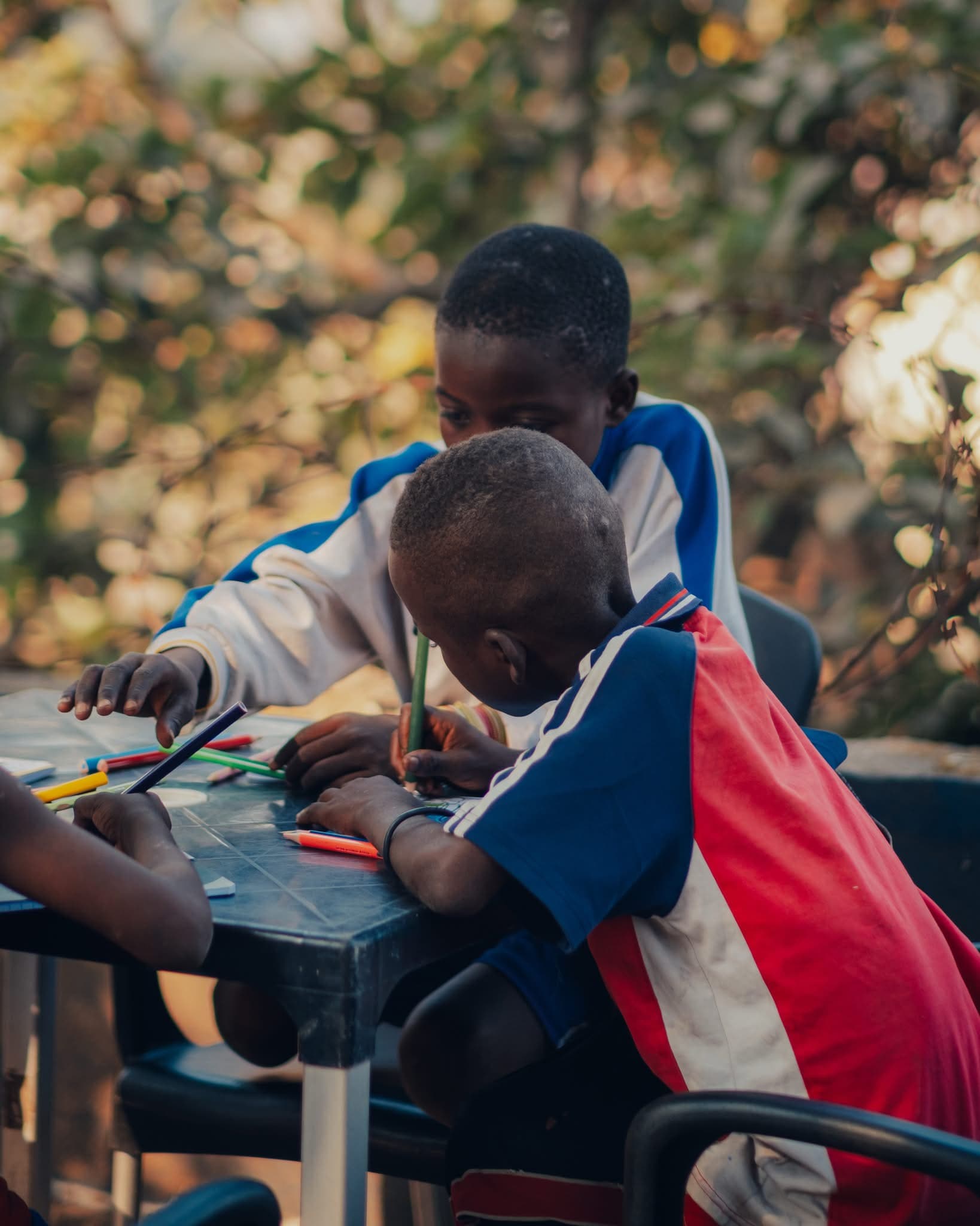 Deux garçons dessinent à une table en plein air, au centre One Love.